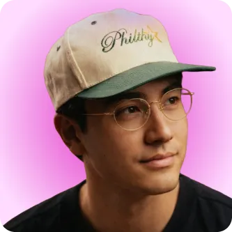 Man with glasses wearing a beige and green cap set against a pink gradient background.