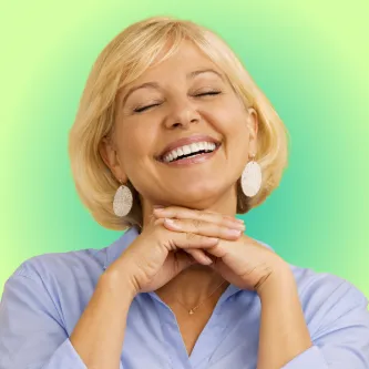 Smiling blonde woman with closed eyes resting her chin on clasped hands against a green gradient background.