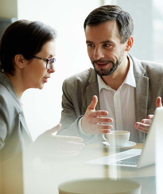 Two professionals discussing something in front of a laptop with a coffee cup on the table.