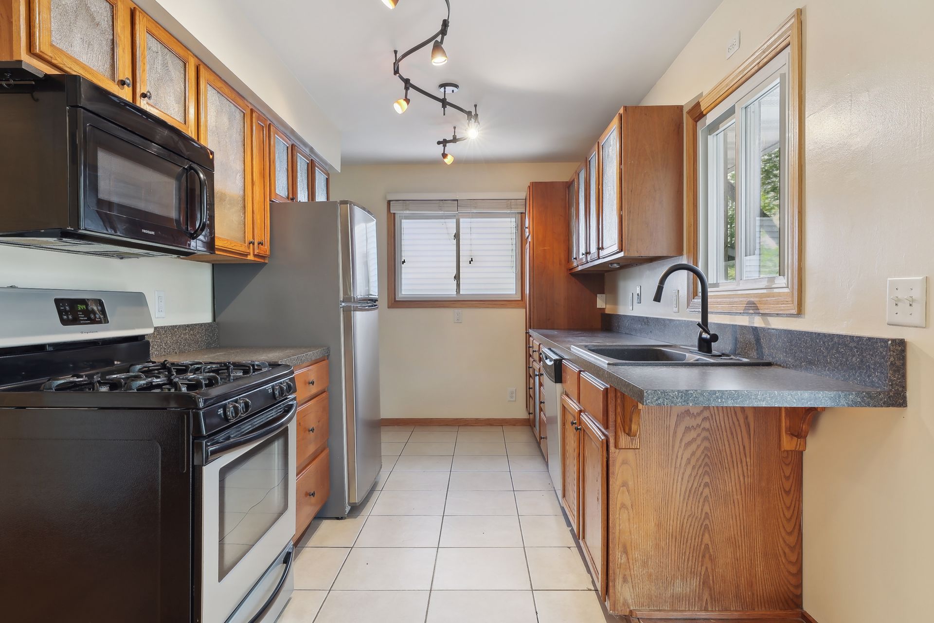 Kitchen with wooden cabinets, black gas stove and microwave, stainless steel refrigerator, and a window above the sink.
