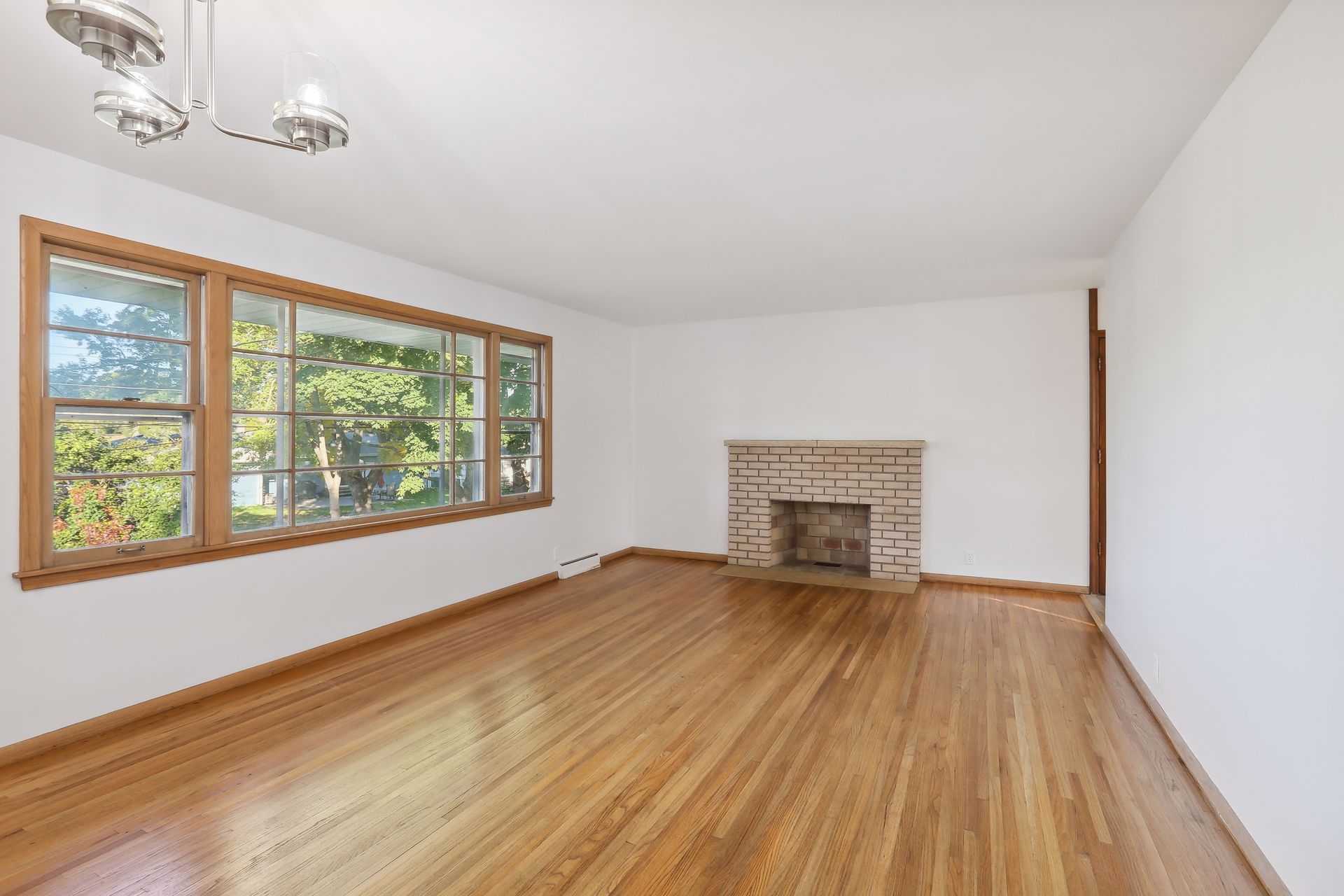 Empty living room with hardwood floors, a staircase with wooden railing, and a wooden door entrance with a tiled entryway.
