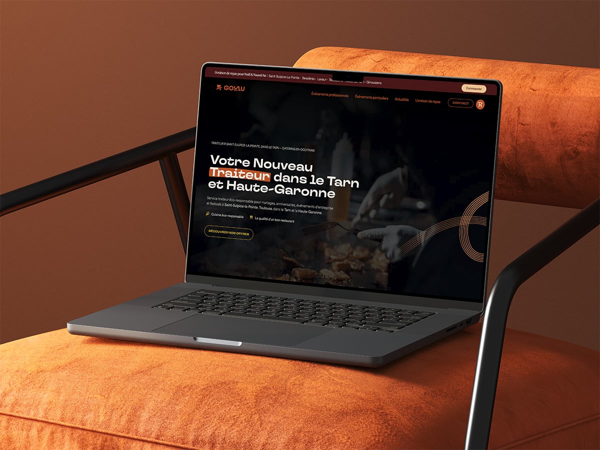 Ordinateur portable affichant la page d’accueil du site Goulu Traiteur, posé sur un fauteuil orange dans une ambiance chaleureuse.