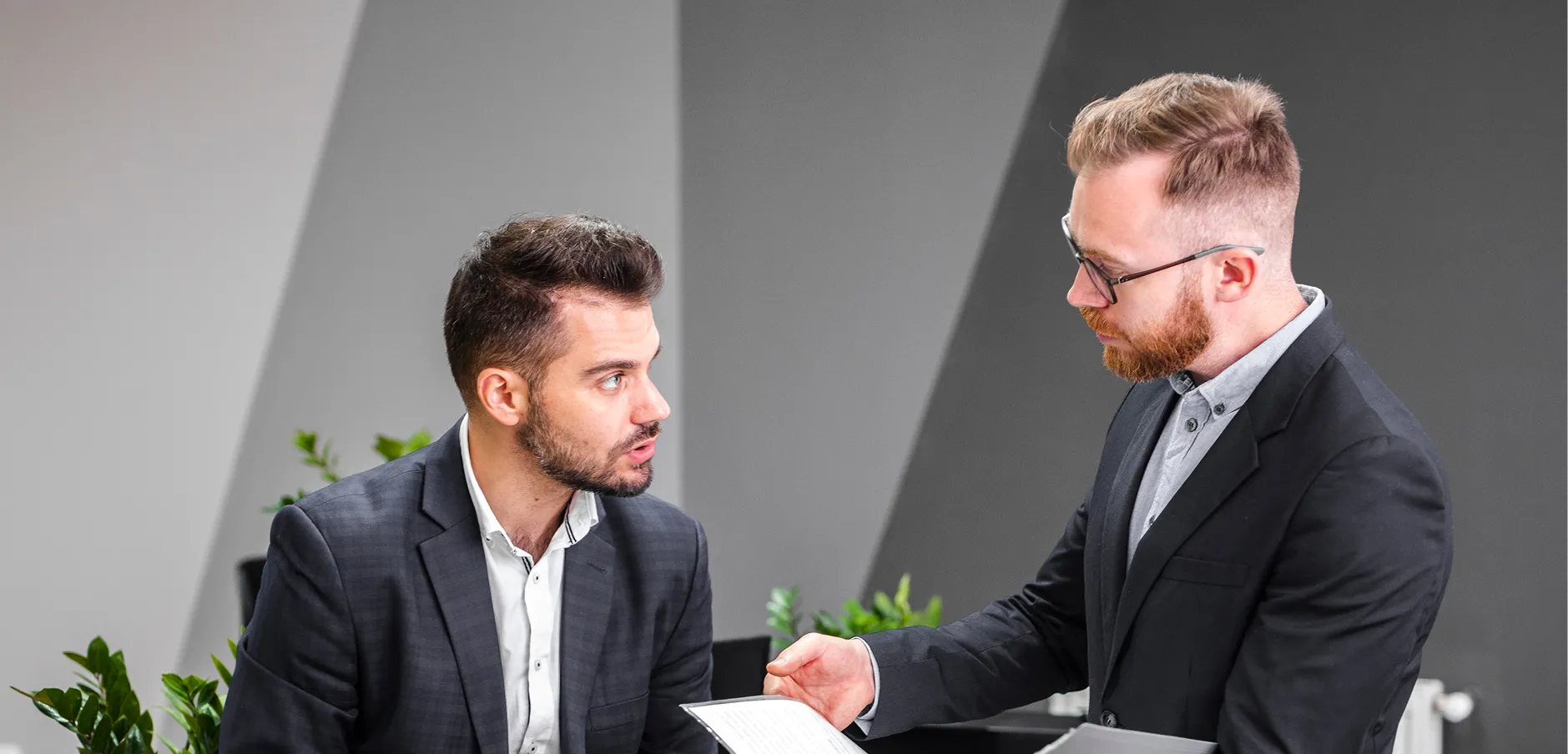 Two men in suits having a serious discussion, one holding a document.