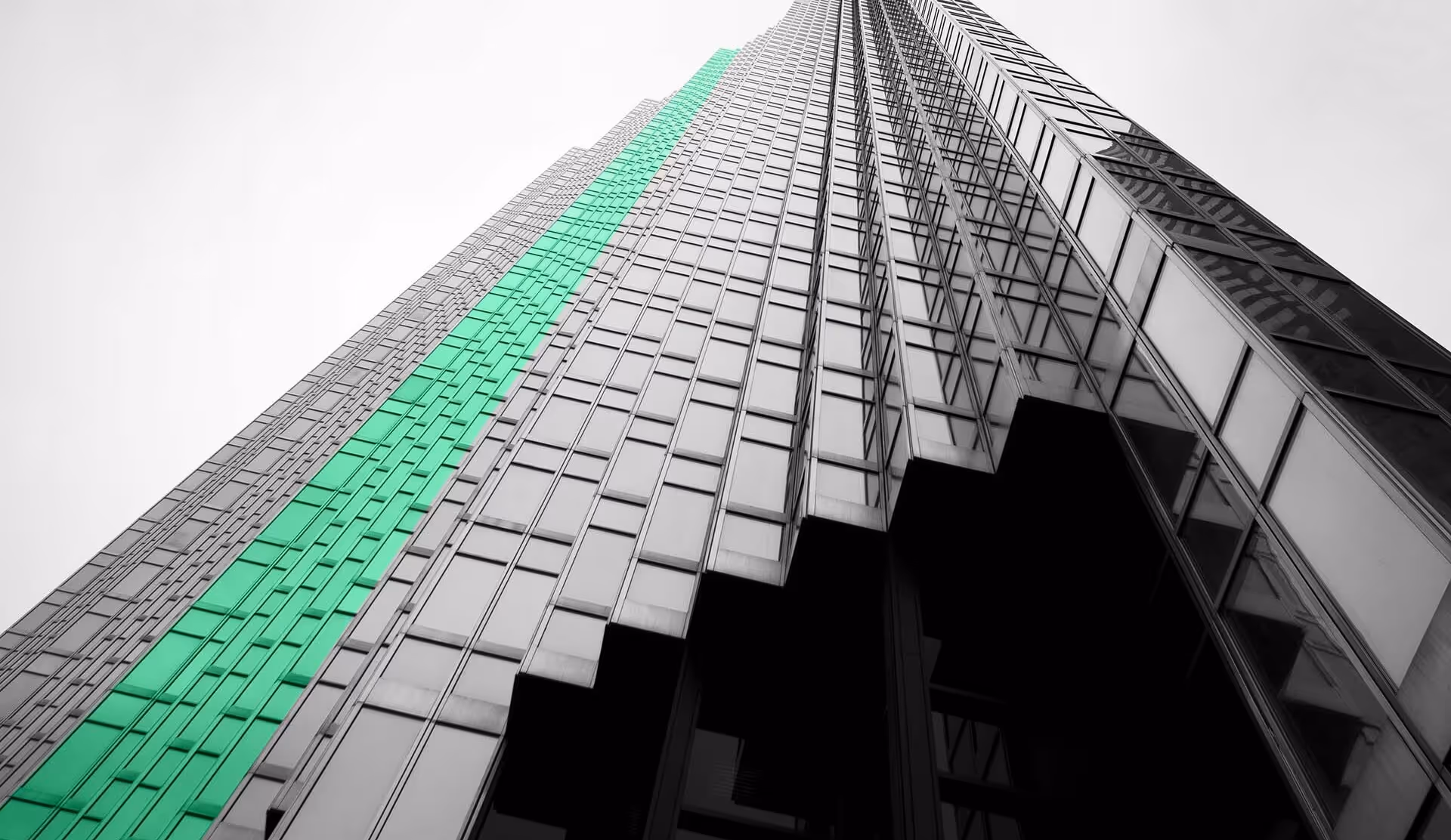 Low-angle view of a modern glass skyscraper with a vertical strip of windows highlighted in green.