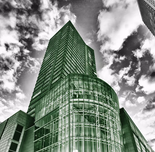Low-angle view of a modern glass and steel skyscraper against a cloudy sky.
