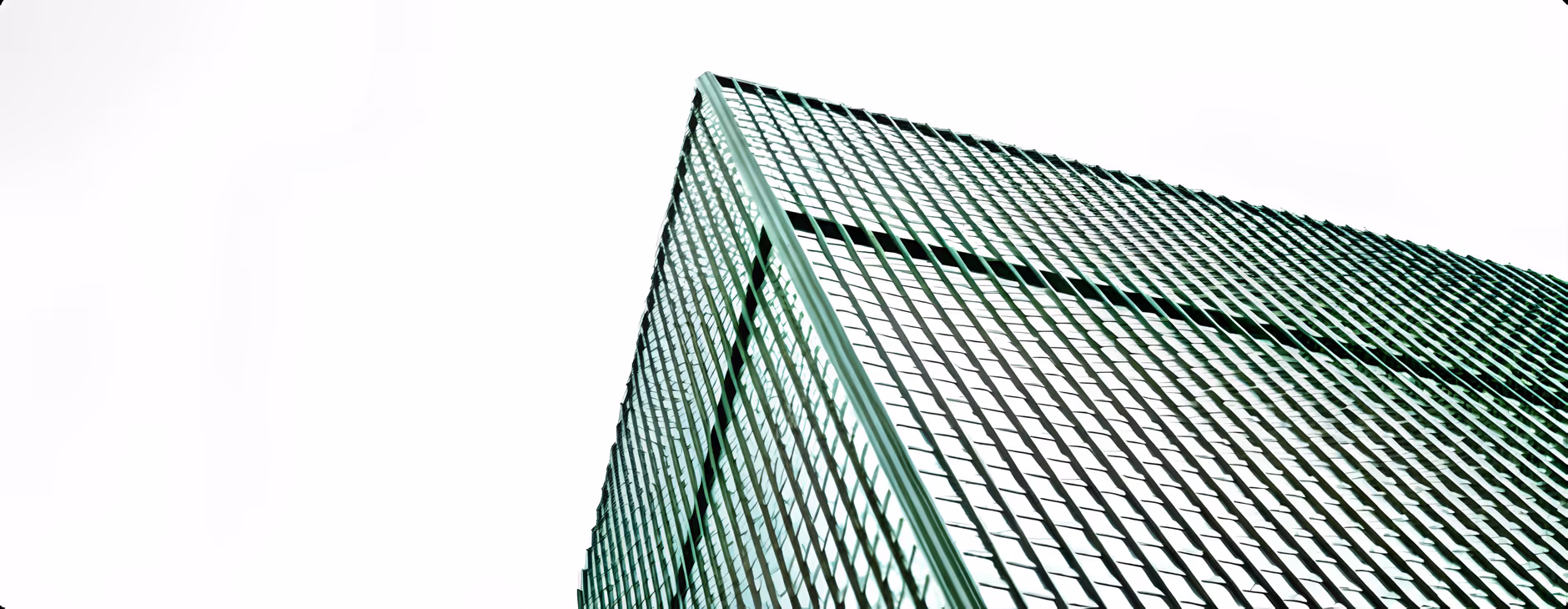 Upward view of a modern glass skyscraper with reflective windows and crisscrossing metal frames against a white sky.