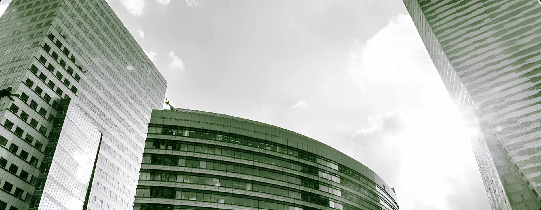 Low-angle view of modern glass office buildings with sun glare and cloudy sky.