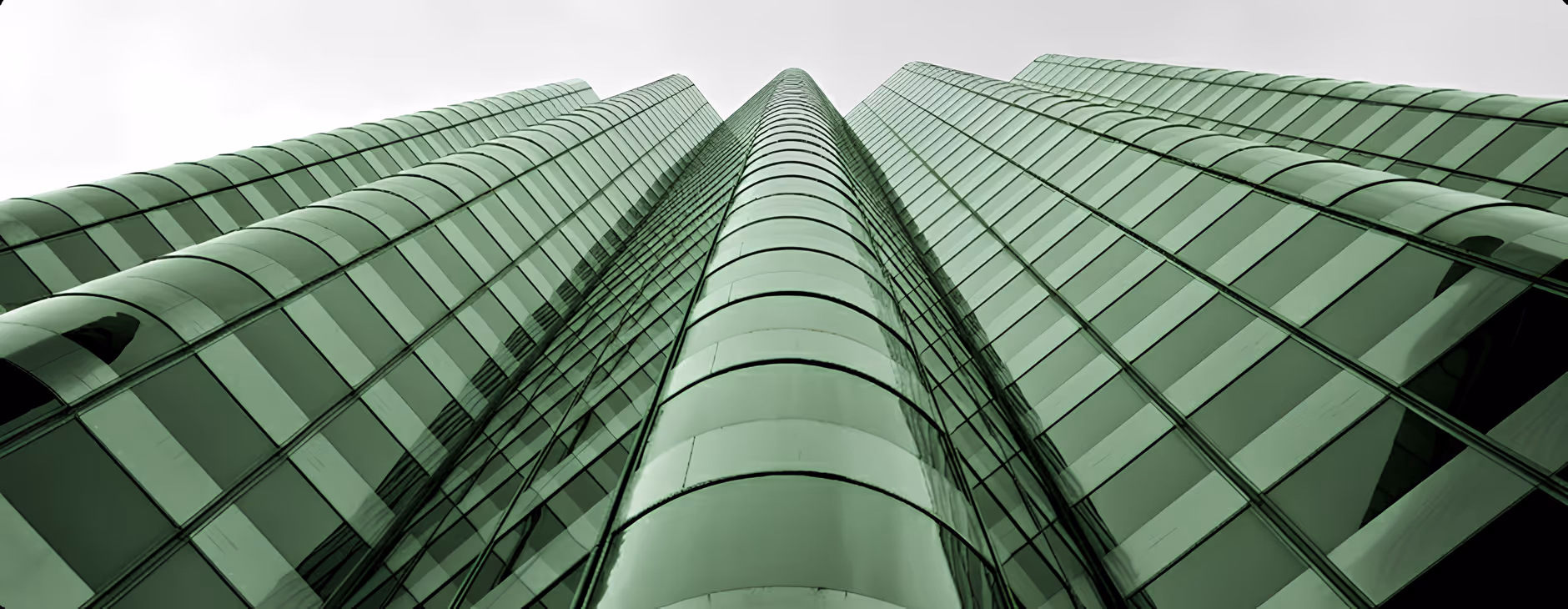 Low-angle view of a modern high-rise building with green-tinted glass windows and curved architectural features.