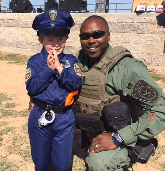 Officer kneeling beside a young child dressed in a police uniform during a community event.