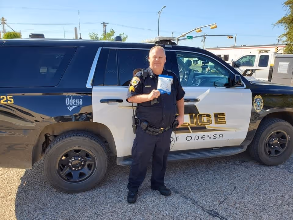 Officer standing beside an Odessa Police patrol SUV holding a small certificate or card.