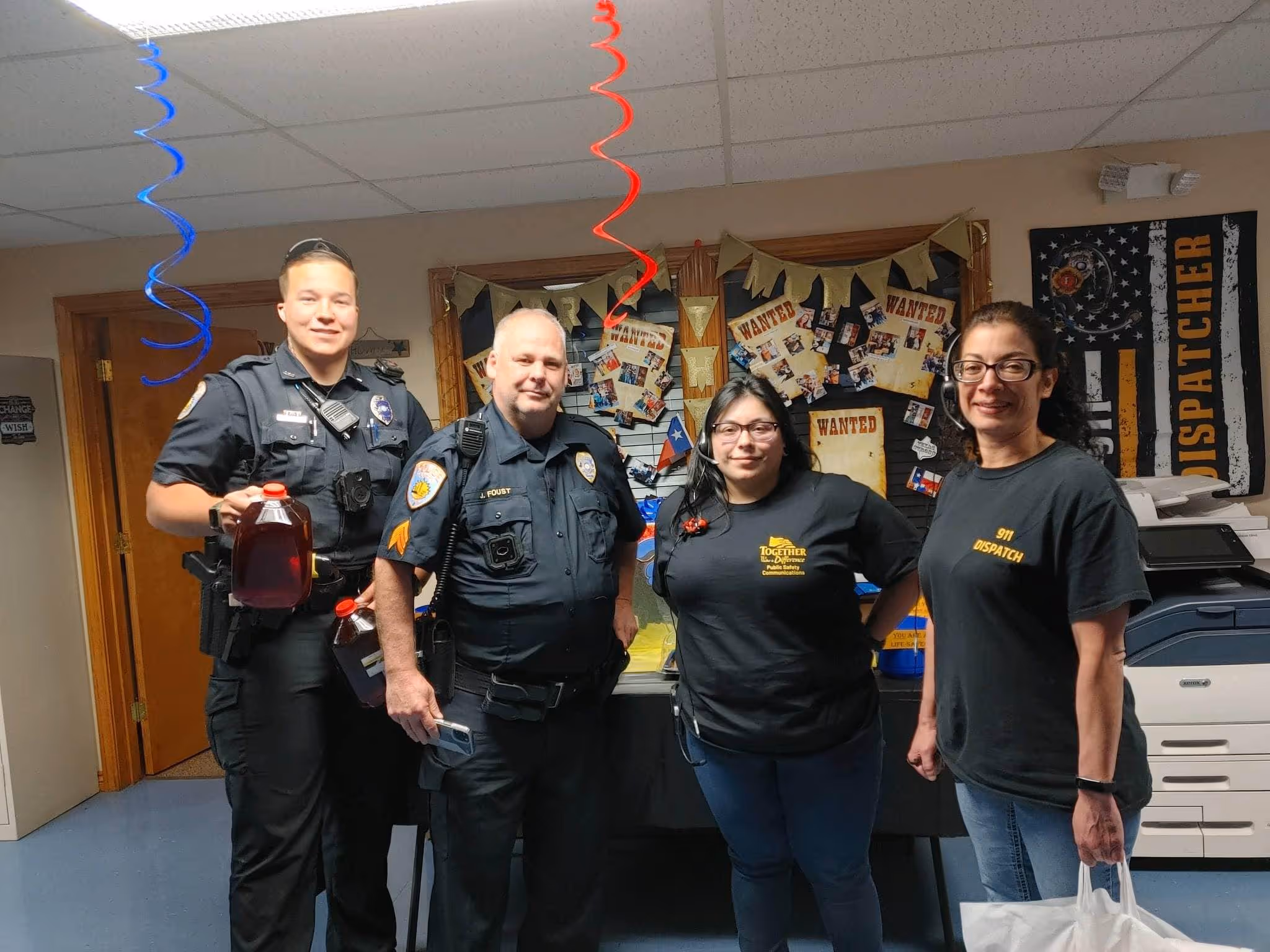 Group of officers and dispatch staff standing together inside a decorated office during an appreciation event.