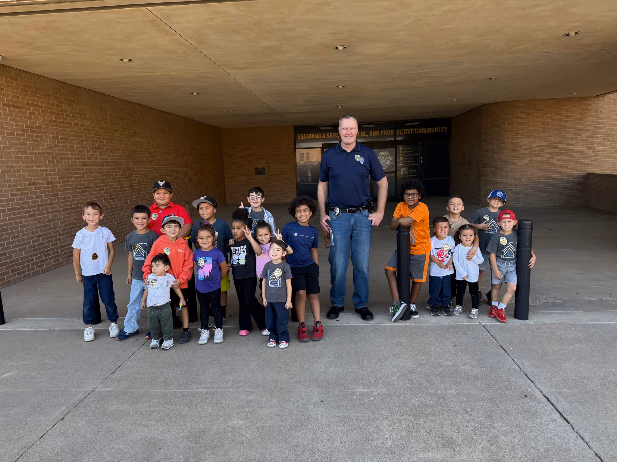 Officer standing outside a building with a large group of smiling children during a community visit.