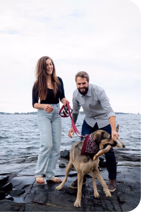 Smiling couple with dog on rocky shore