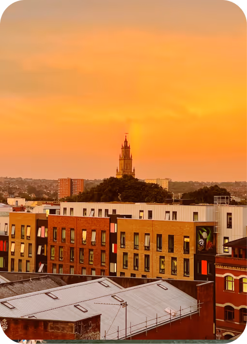 Cityscape with mixed modern and older buildings under an orange sunset sky.