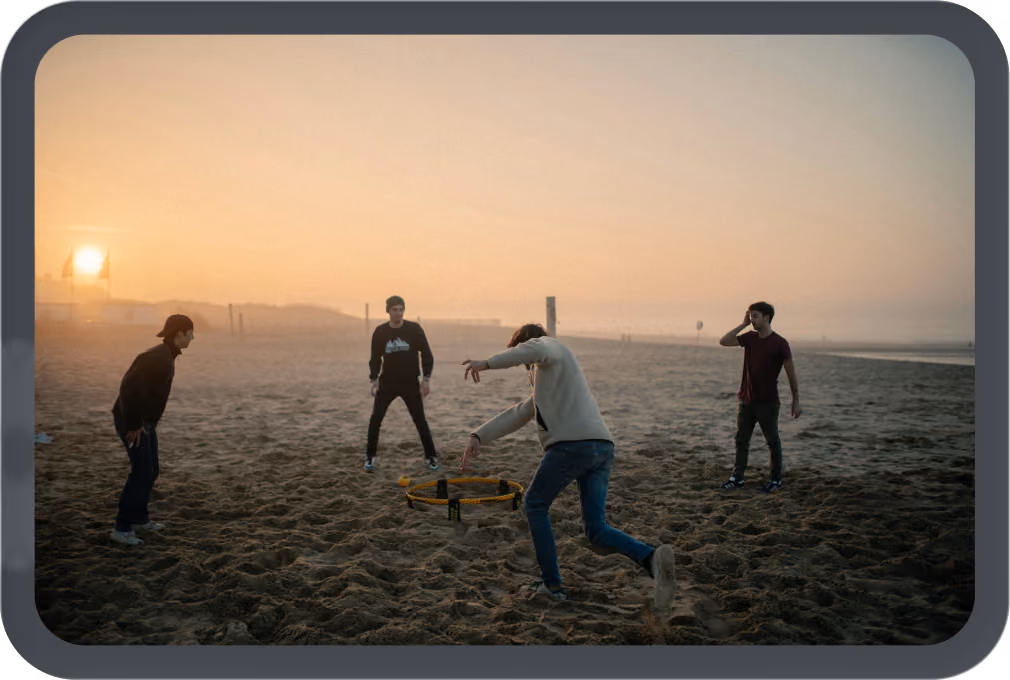 Four people playing spikeball on a sandy beach at sunset with a hazy sky.
