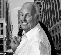 Smiling man in a white shirt holding a jacket over his shoulder in an urban street setting.