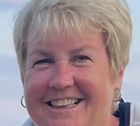 Smiling woman with short blonde hair and hoop earrings against a light sky background.