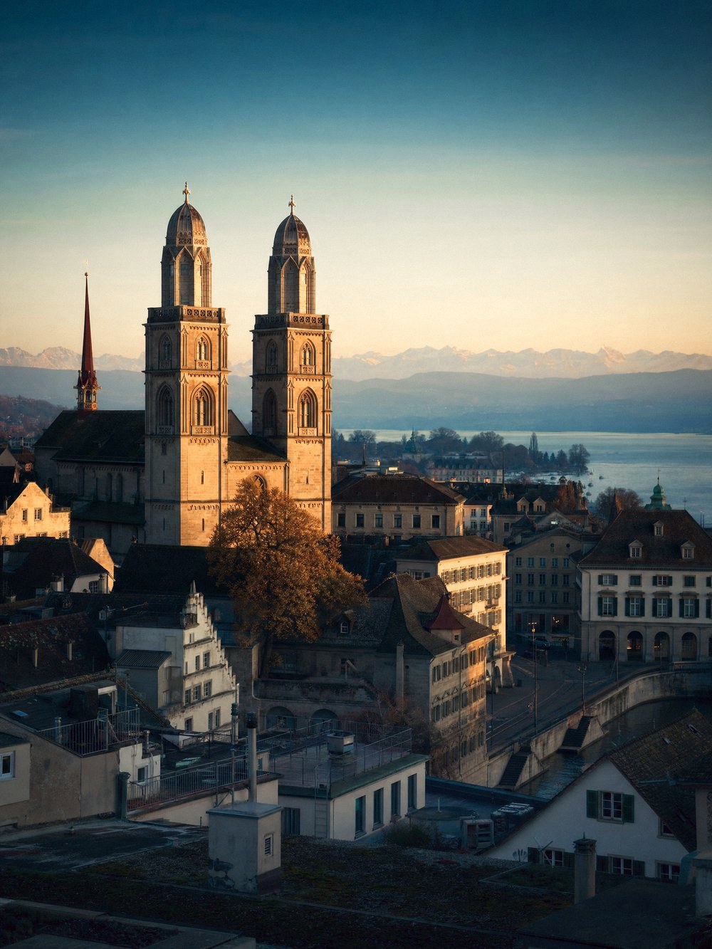 Rooftop view across the old town of Zurich at golden hour, the twin towers of the Grossmunster above the lake