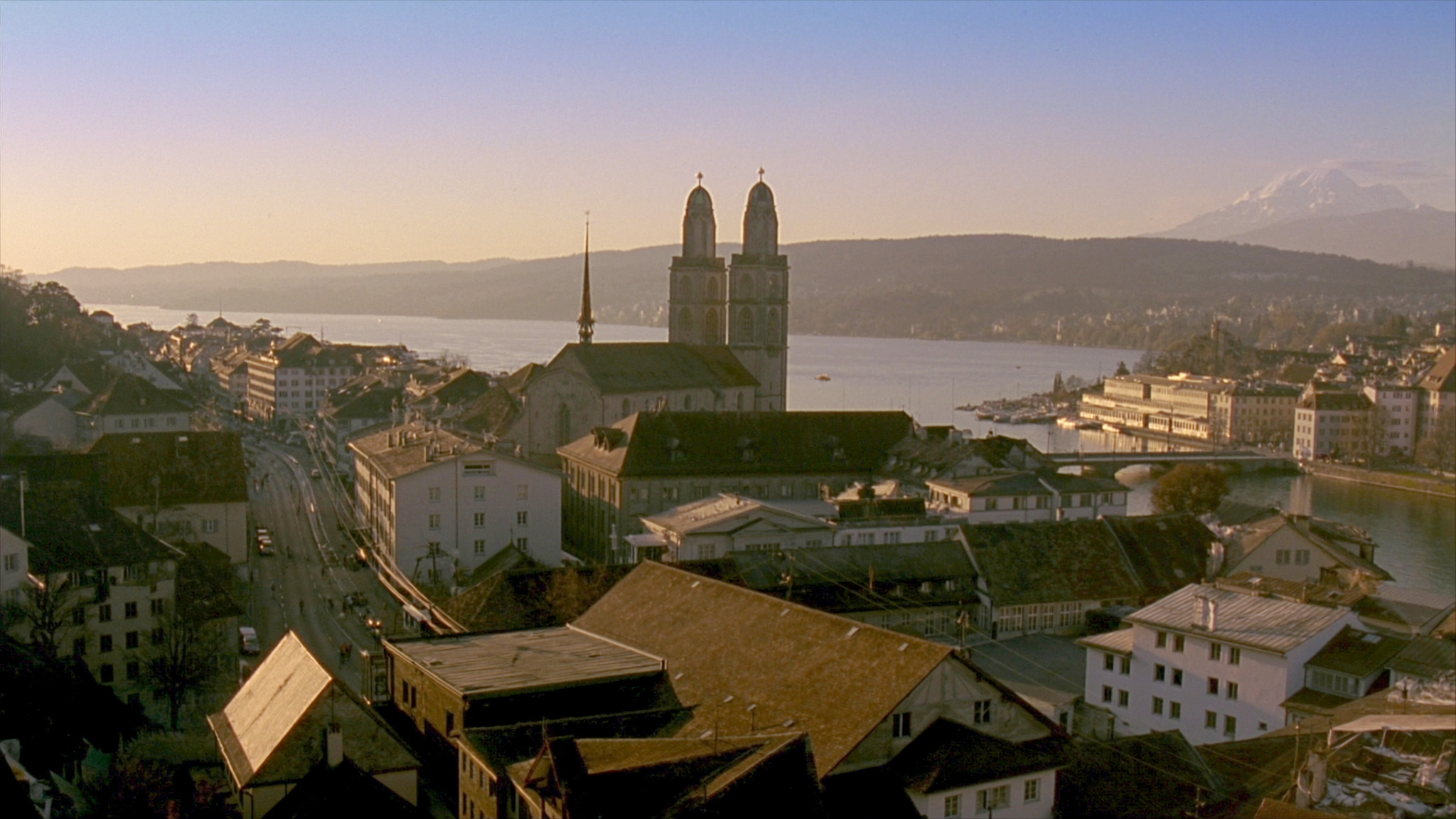 Zurich old town at golden hour, the twin towers of the Grossmunster above the rooftops with the lake and the Alps beyond