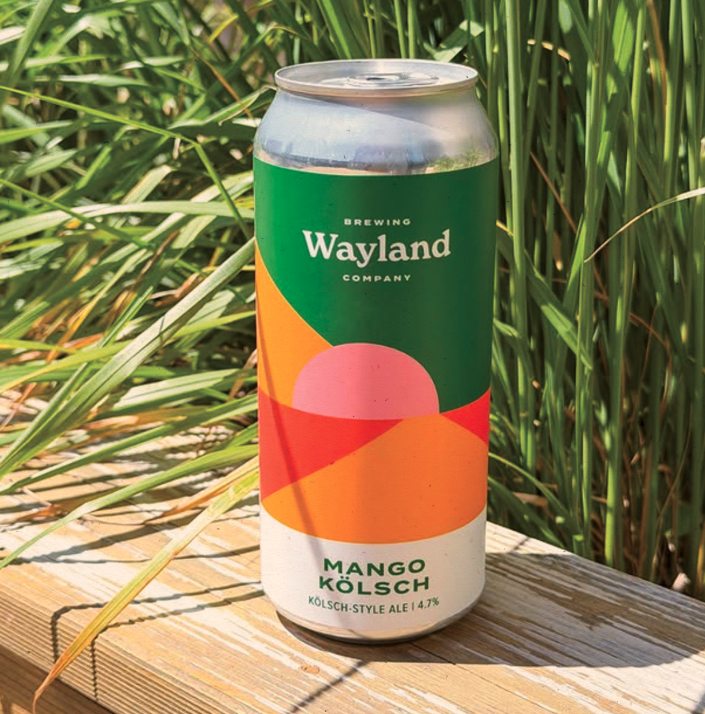 Can of Wayland Brewing Company's Mango Kölsch ale with colorful abstract label on wooden surface outdoors.