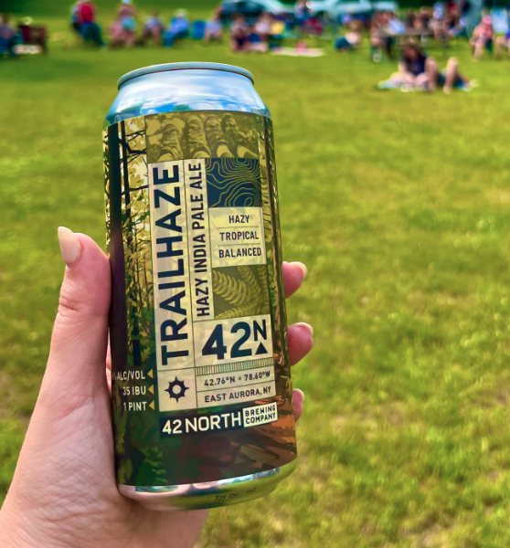 Hand holding a can of Trailhaze Hazy India Pale Ale by 42 North Brewing Company on green grass.