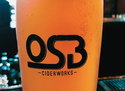 Close-up of a glass filled with an orange beverage labeled OSB Ciderworks.