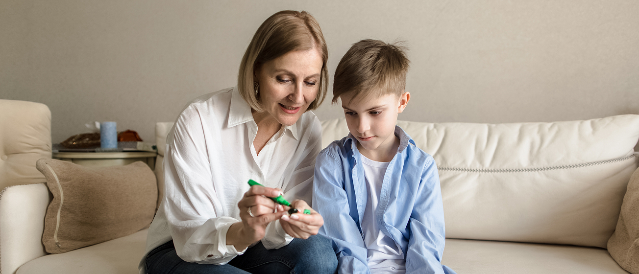 Woman painting a young boy's nails as they sit together on a beige couch.