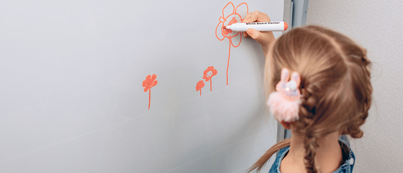 Young girl with braided hair drawing orange flowers on a whiteboard with an orange marker.
