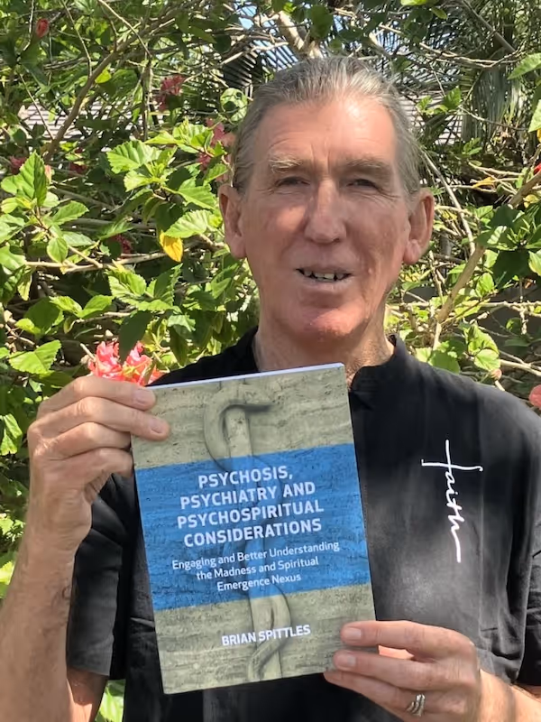Brian Spittles holding his book Psychosis, Psychiatry and Psychospiritual Considerations