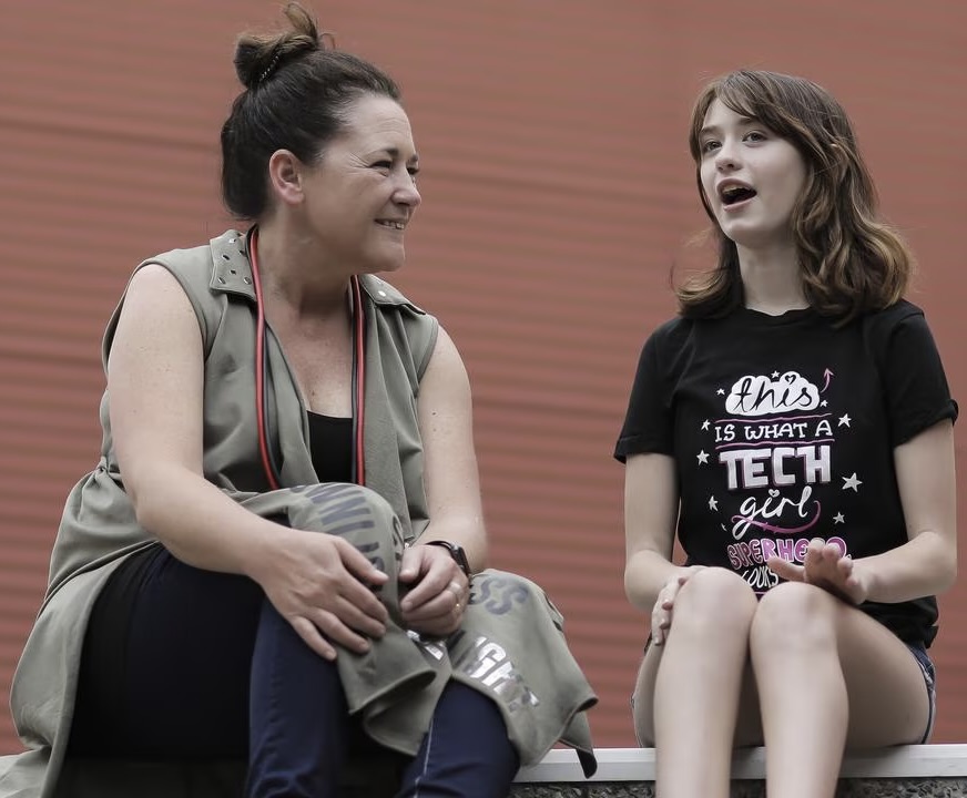 Jenine chats with a young girl proudly wearing a Tech Girls T-shirt that says, "This is what a tech girl superhero looks like."