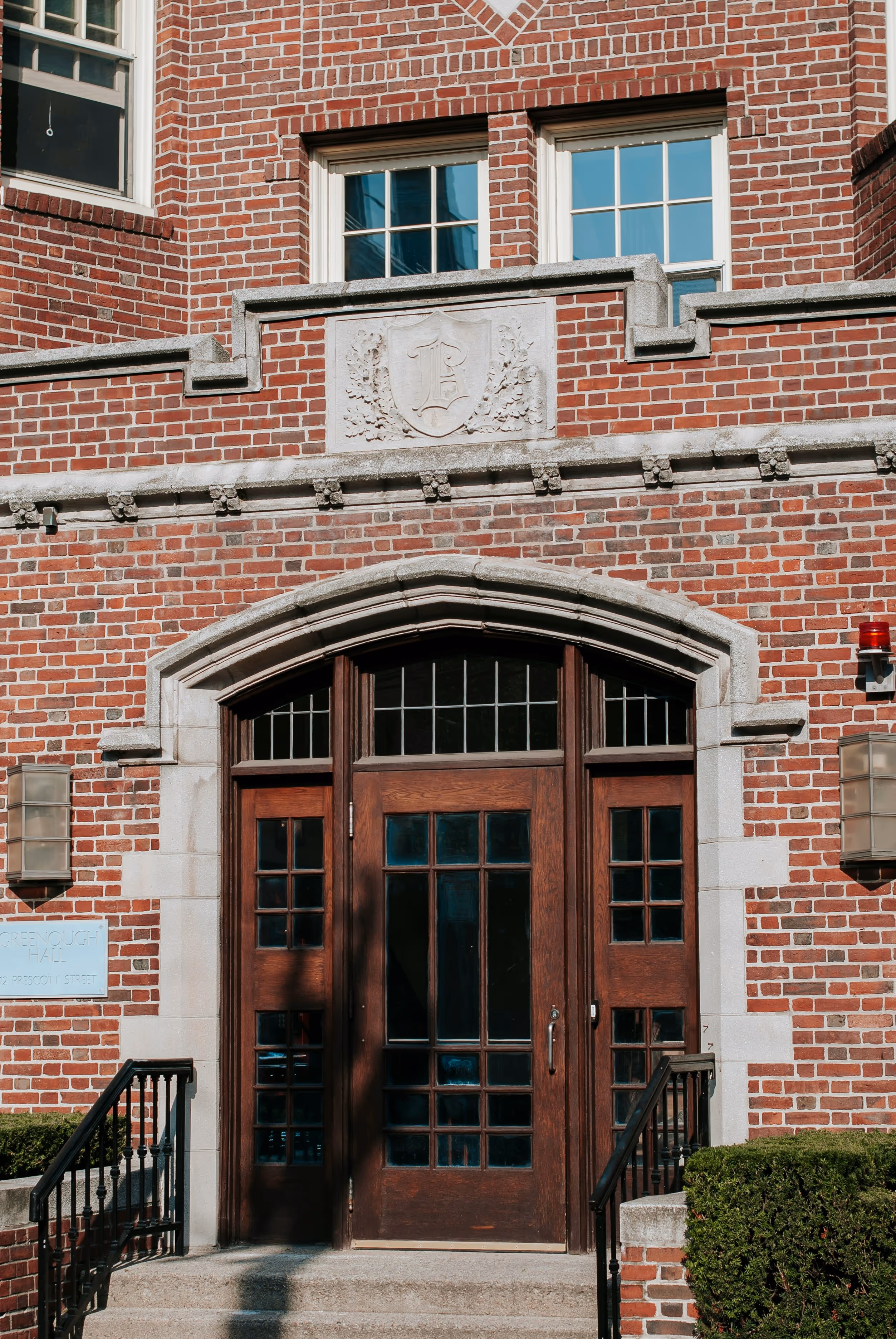 Wooden double door entrance with arched stone frame on a red brick building with two windows above.