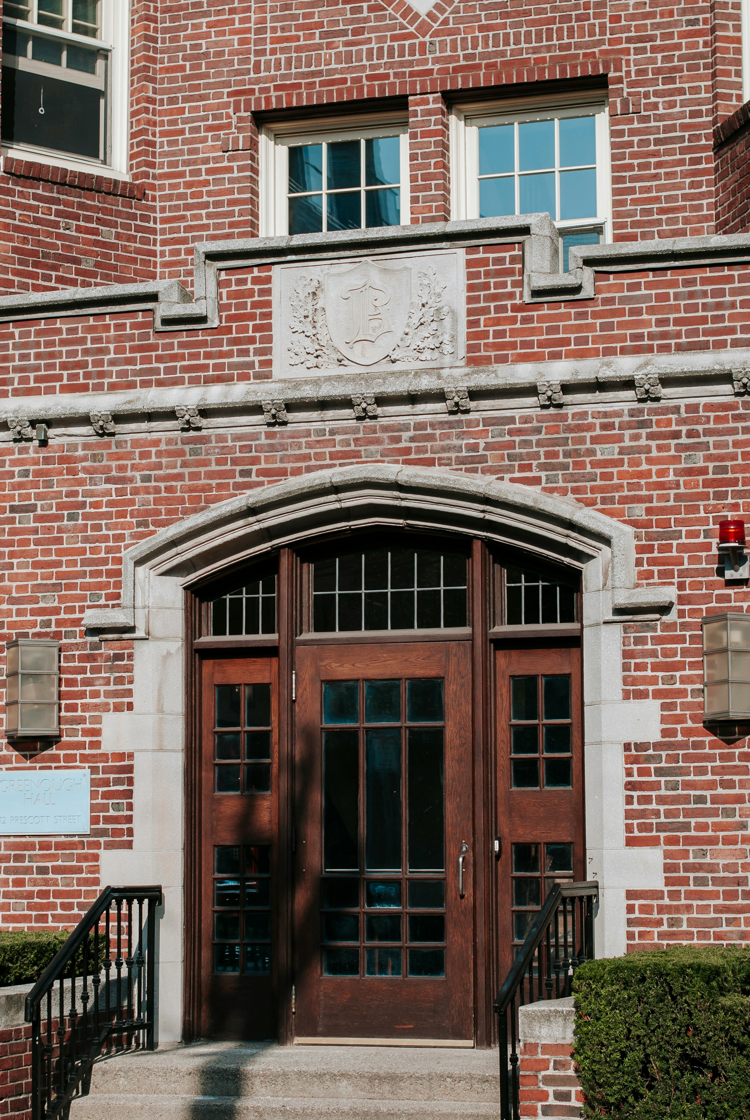 Wooden double door entrance with arched stone frame on a red brick building with two windows above.