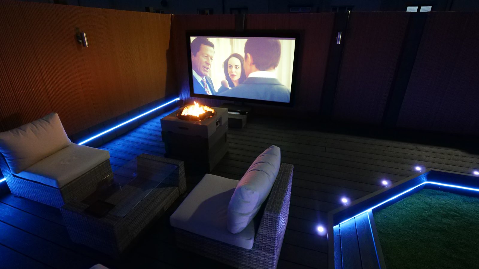 Finished garden cinema seating area with fire pit and screen at night
