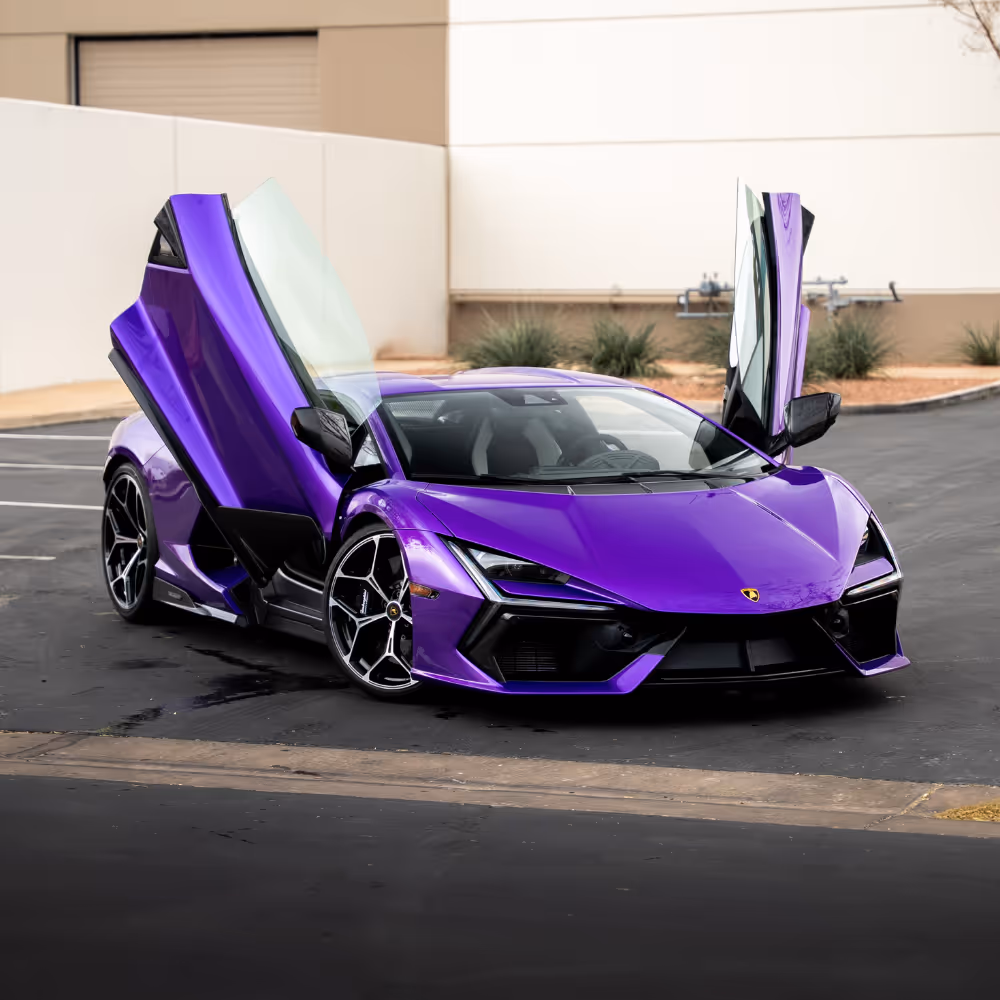Purple Lamborghini sports car with scissor doors open parked on asphalt near a building.