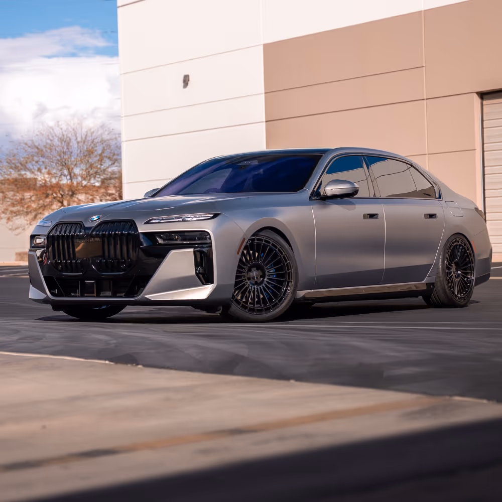 Silver BMW luxury sedan with black detailing and tinted windows parked in front of a beige building.
