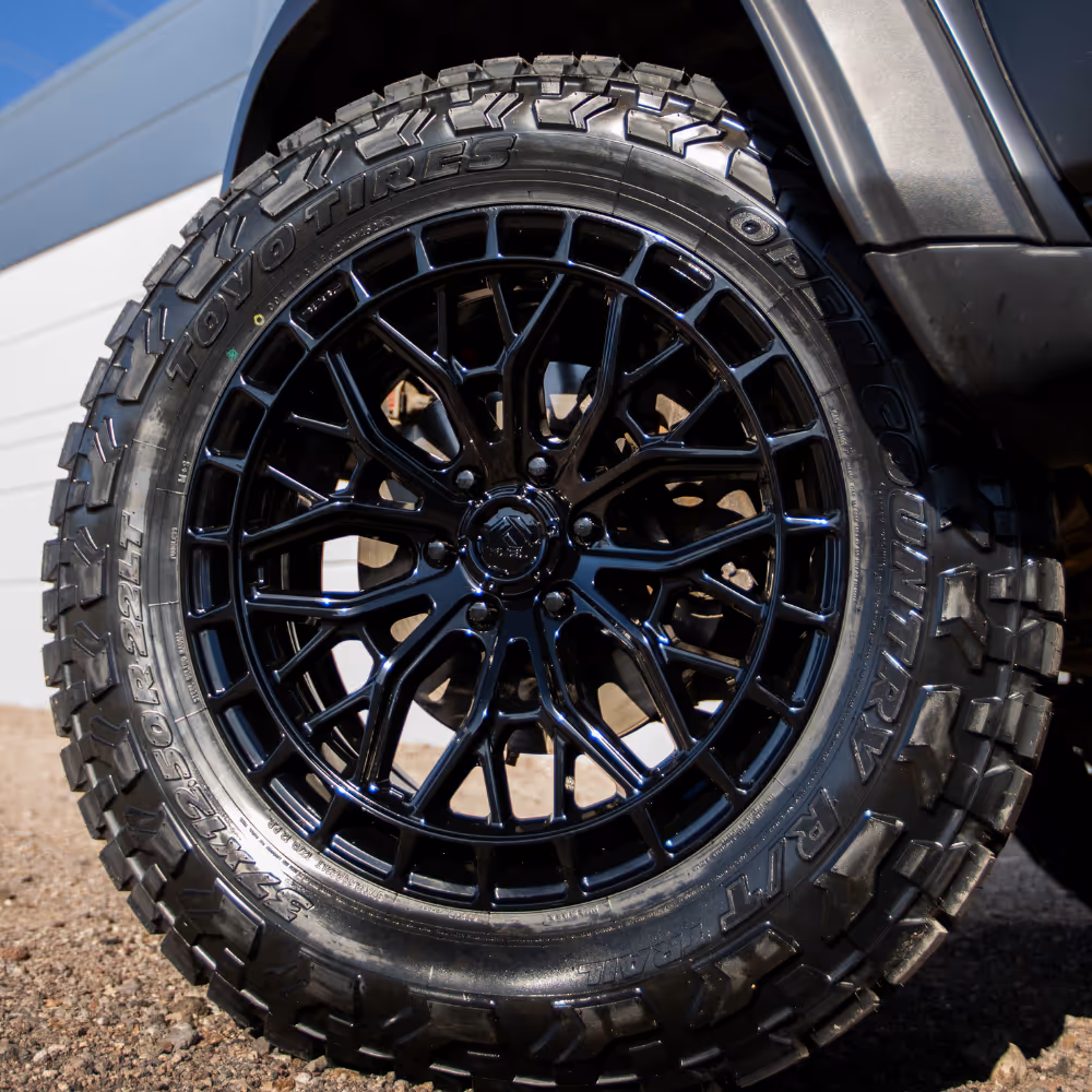 Close-up of a black, intricate multi-spoke off-road wheel with Toyo Open Country R/T tire mounted on a vehicle.