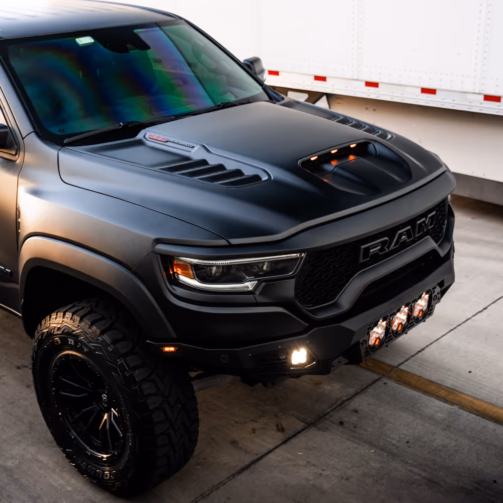 Front side view of a matte black RAM pickup truck with prominent hood vents and off-road tires.
