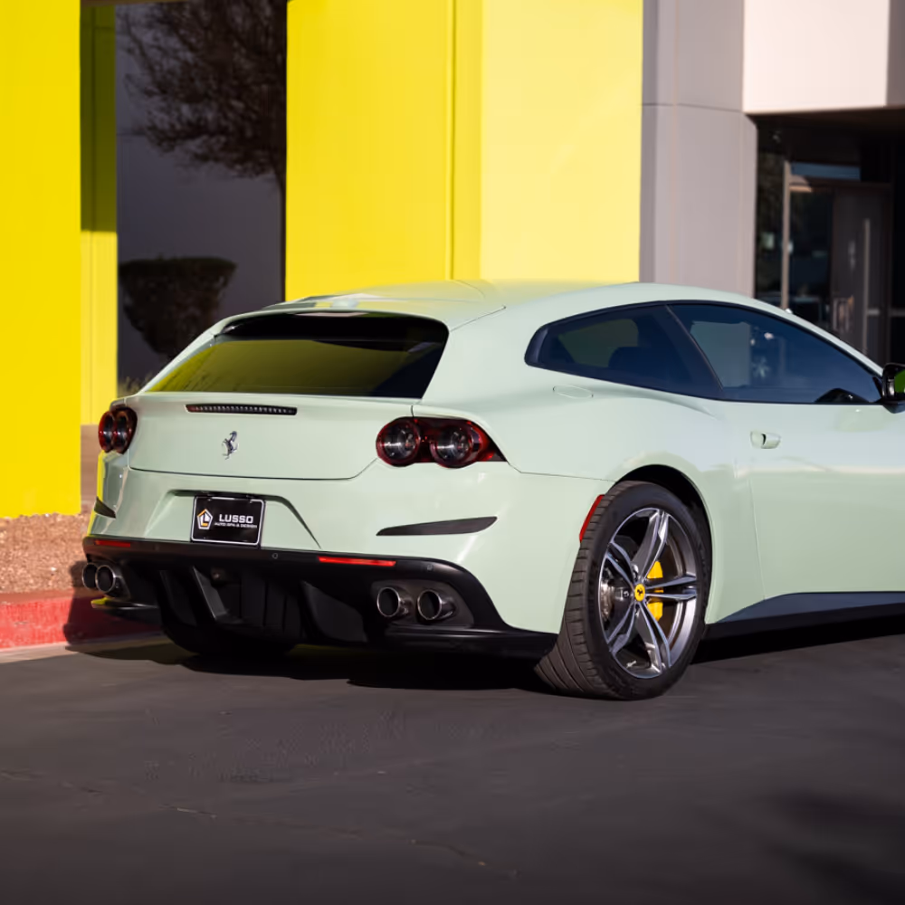 Rear-side view of a light green Ferrari shooting brake parked near a bright yellow building.