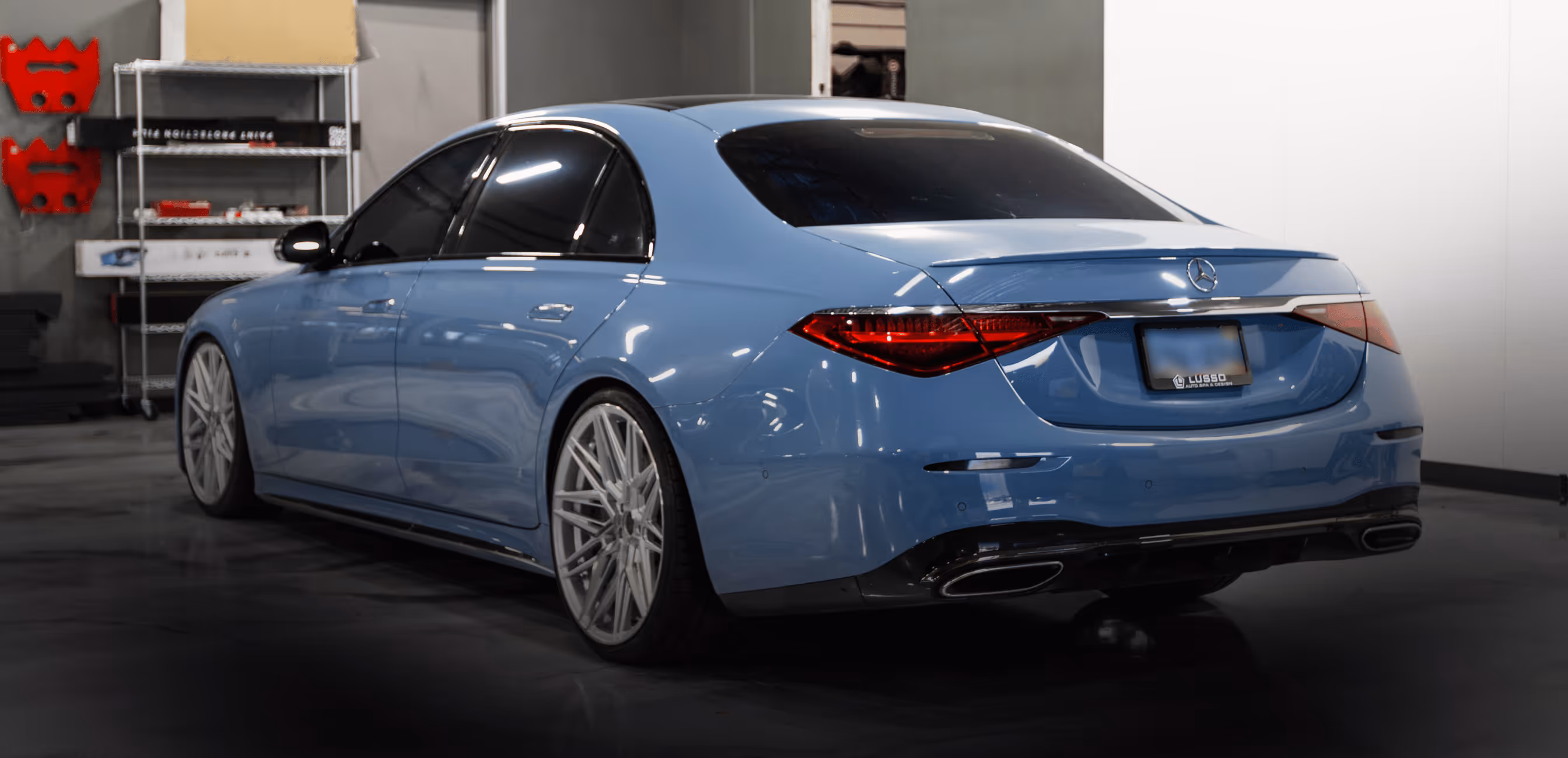 Rear side view of a blue Mercedes-Benz sedan with tinted windows inside a garage.