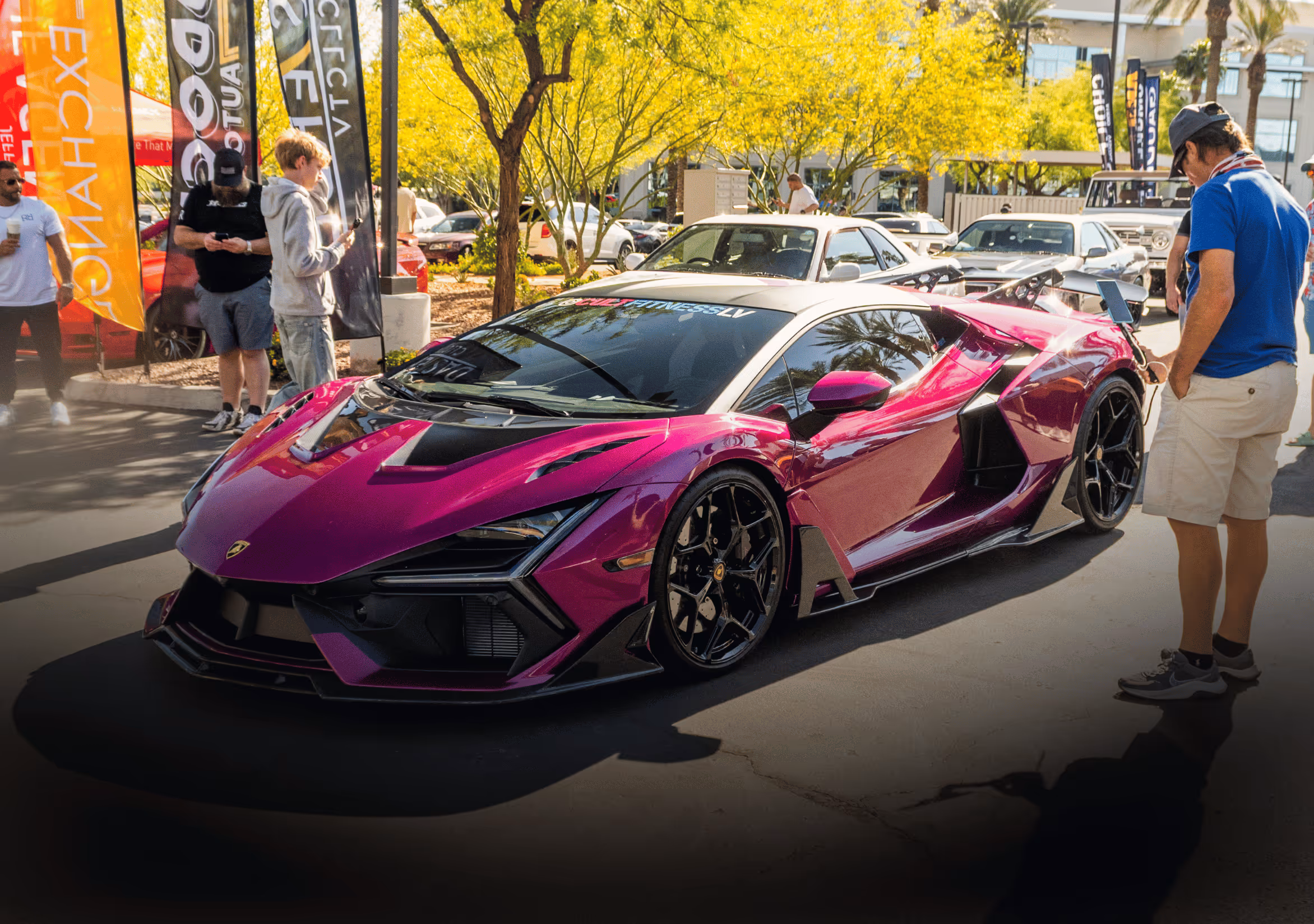 Shiny purple Lamborghini sports car parked outdoors at a car show with people observing it.