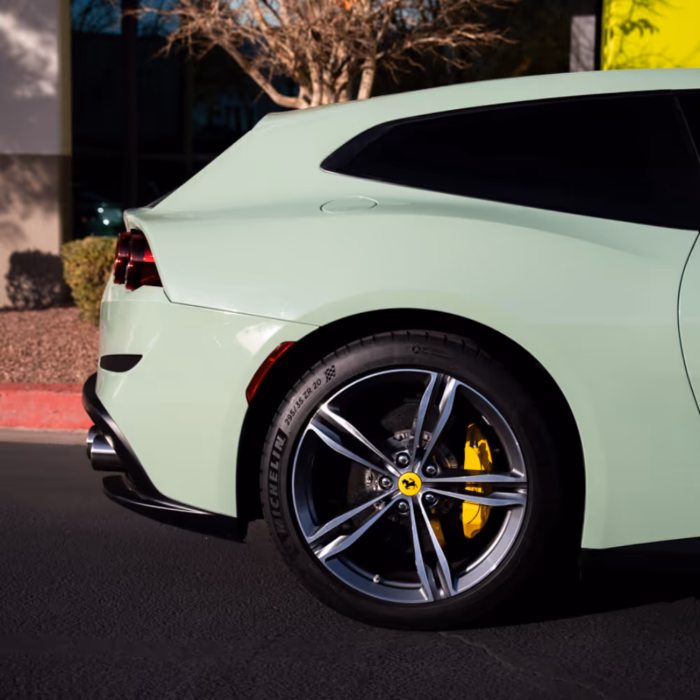 Rear side view of a light green Ferrari with yellow brake calipers and Michelin tires parked on asphalt.