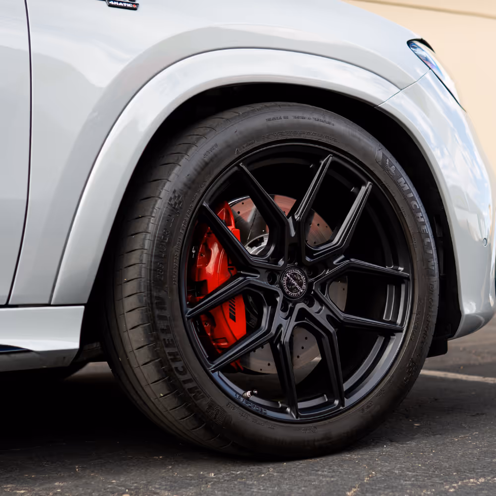 Close-up of a black alloy wheel with a red brake caliper on a silver luxury car.