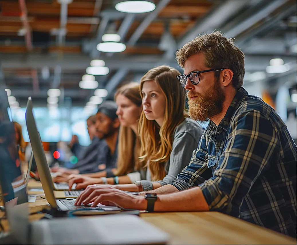 Group of young professionals working intently on laptops in a modern, well-lit office.