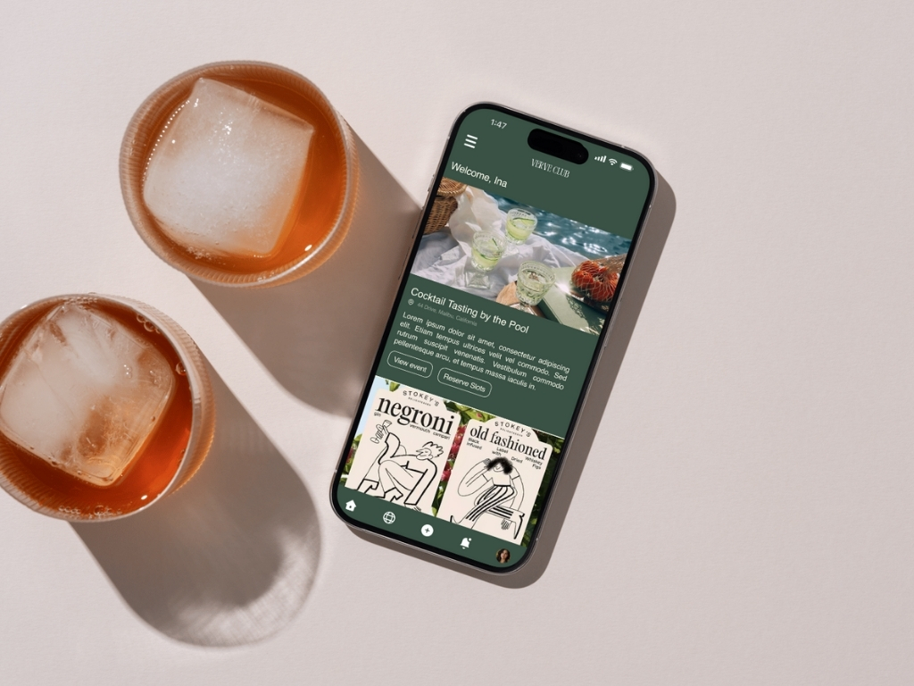 Smartphone displaying a cocktail tasting event app next to two glasses with ice cubes and iced drinks on a light surface.