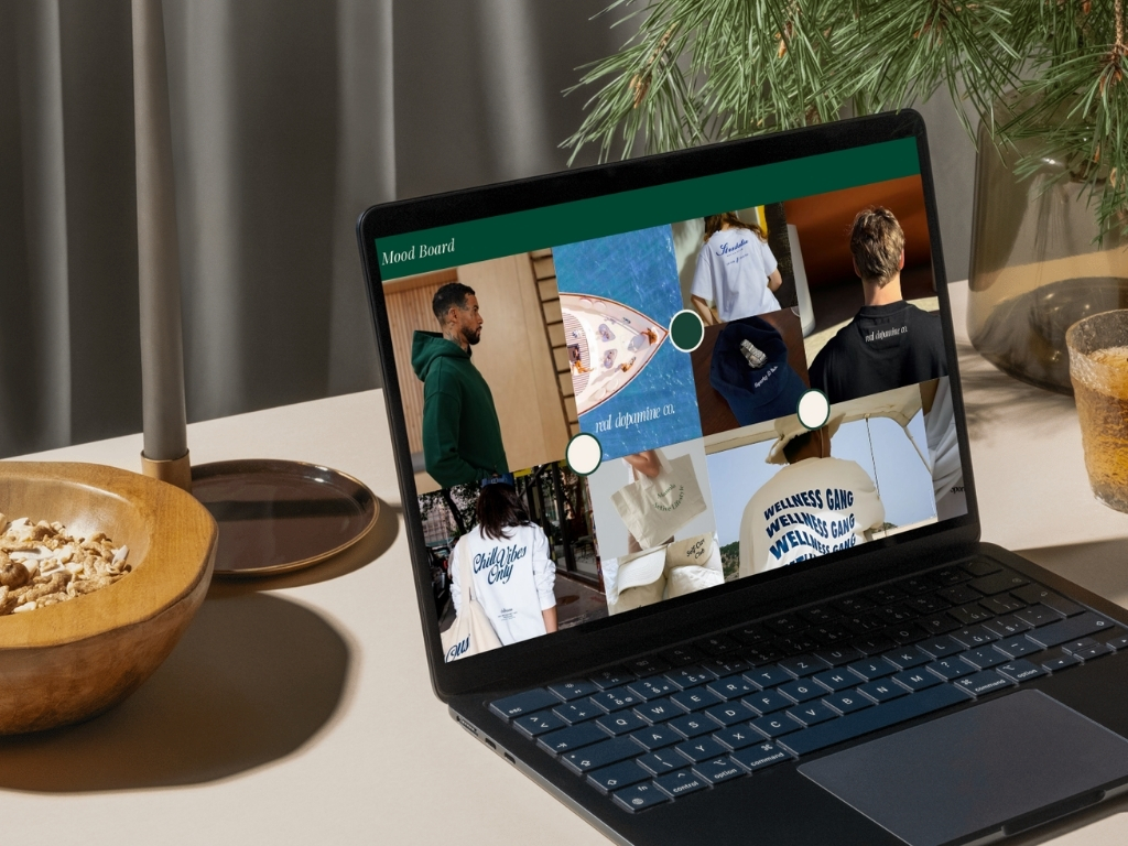Laptop on a table displaying a mood board collage with images of people wearing casual hoodies and tees featuring text like 'Chill Vibes Only' and 'Wellness Gang.'