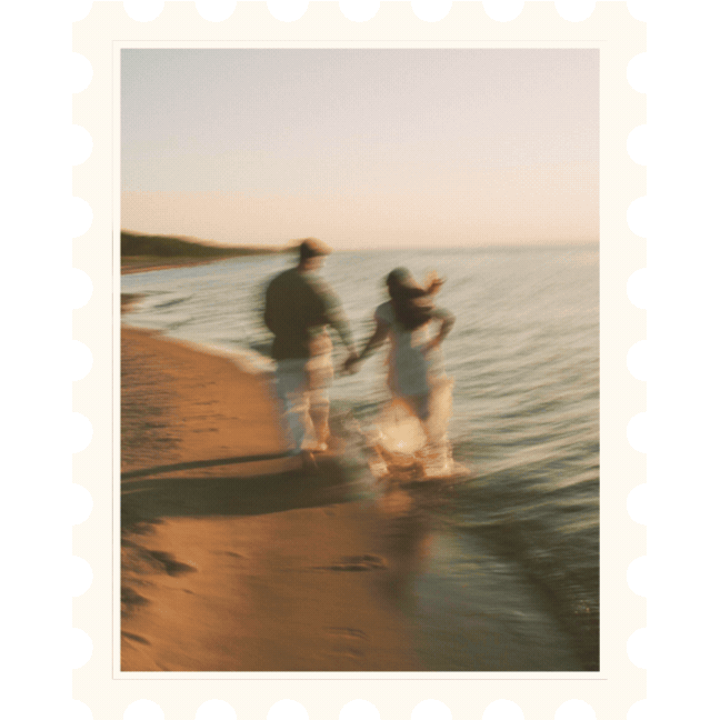 Blurred image of a couple holding hands walking along a beach shoreline at sunset or sunrise, with waves gently touching their feet.