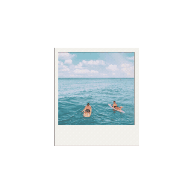 Two people on surfboards floating in calm ocean water under a partly cloudy blue sky.