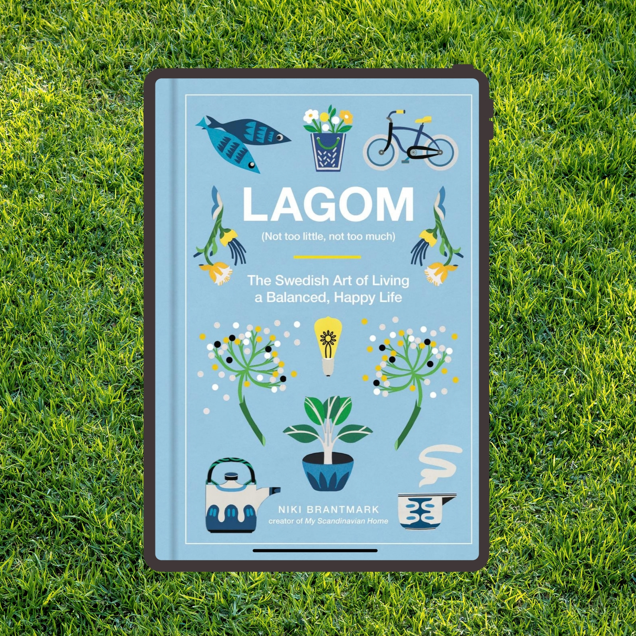 Book cover of 'Lagom (Not too little, not too much)' featuring illustrations of two fish, a basket with flowers, a bicycle, yellow flowers, abstract floral designs, a potted plant, a teapot, and a steaming cup, with the subtitle 'The Swedish Art of Living a Balanced, Happy Life' by Niki Brantmark.