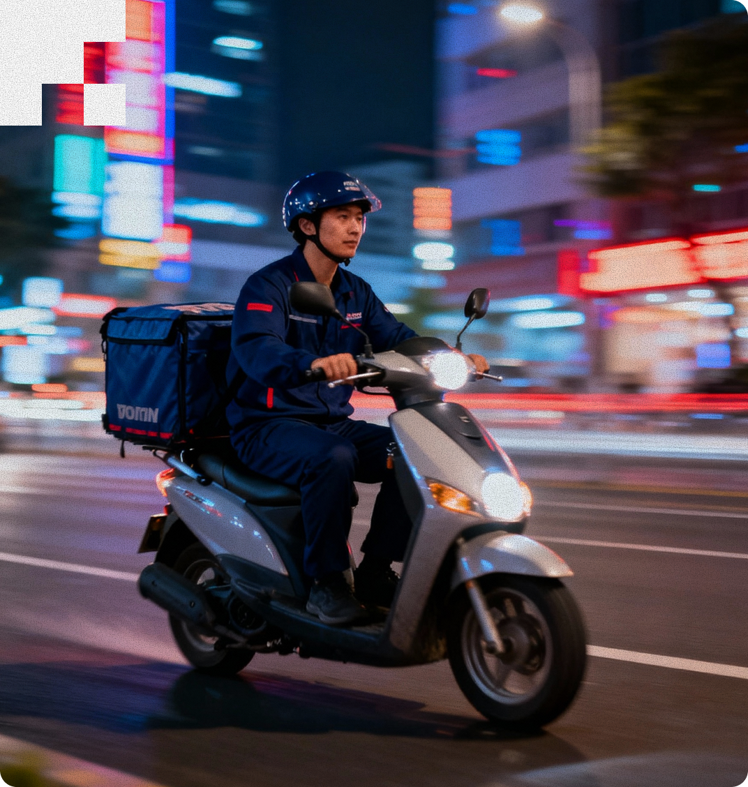Delivery person wearing helmet and navy uniform riding a scooter with delivery box on city street at night.
