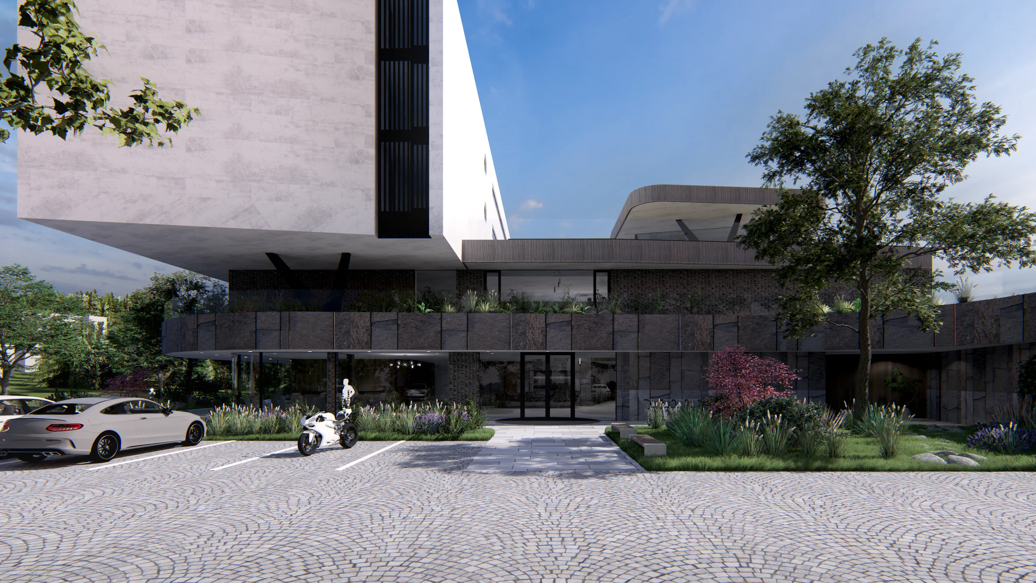 Aerial view of a modern building with green roofs next to a small lake, surrounded by trees and other buildings, including roads with cars and a bus.